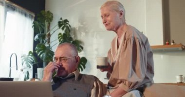 Mutlu gülümseyen emekli çift, 70 'li yaşlarda beyaz erkek ve kadın evdeki kanepede dizüstü bilgisayar alışverişi yapıyor..