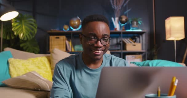 Ung glad gen-z svart manlig student i glasögon med bärbar dator för att studera online uttrycker olika känslor på mysiga hem. — Stockvideo