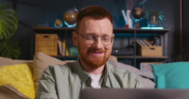 Ung glad smart vit rödhårig frilansande affärsman i glasögon med bärbar dator skrivande arbetar i vardagsrummet. — Stockvideo