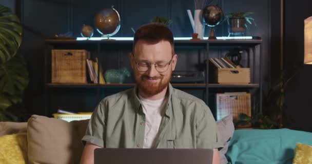 Okos fiatal boldog kaukázusi vörös hajú szabadúszó üzletember szemüveges laptoppal dolgozik online a nappaliban. — Stock videók