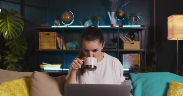 Jobbar hemifrån. Vackra glada unga kaukasiska affärskvinna ler med laptop smuttar kaffe på mysiga vardagsrum — Stockvideo