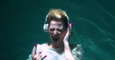 Suyun altında sinematik, neşeli genç bayan heavy metal hayranı kulaklıkla yüksek sesli rock müziği eşliğinde dans ediyor..