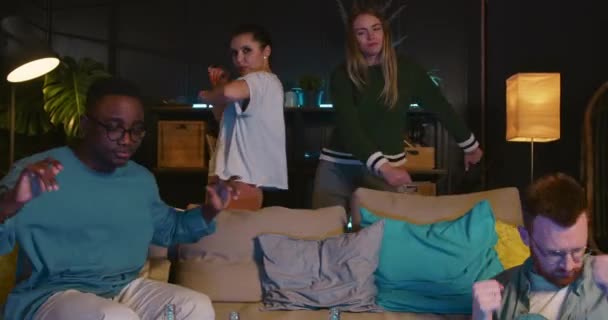 Чотири веселих збуджених молодих щасливих багатоетнічних друзів танцюють разом, розслабляючись сидячи на дивані перед телевізором вдома . — стокове відео