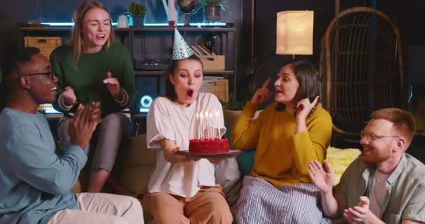 Mooie gelukkige jonge Europese vrouw blaast op verjaardagstaart met kaarsen vieren met plezier diverse vrienden thuis. — Stockvideo