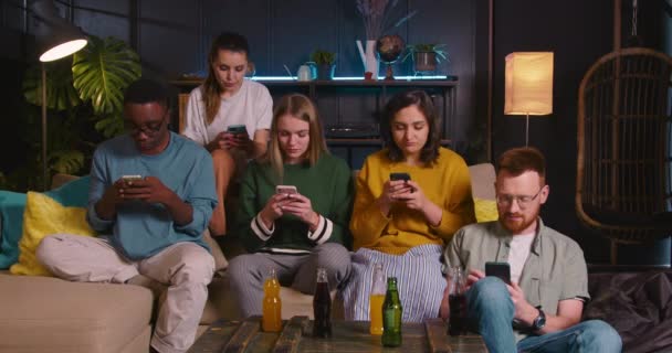 ADICCIÓN DE JUEGOS MÓVILES Grupo de jóvenes amigos multiétnicos felices se sientan en el sofá juntos usando teléfonos inteligentes que no hablan. — Vídeos de Stock