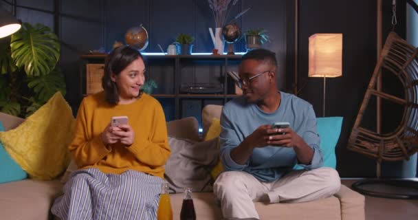 Fiatal boldog többnemzetiségű férfi és nő barátok játék egymás ellen, szörfözés szociális hálózati alkalmazások pihenő otthon — Stock videók