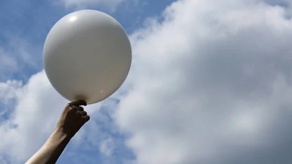 white balloon in hand against the sky