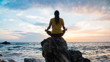 Yoga yapan kadın Lotus pozisyonunda yoga ve meditasyon yapıyor. Akşam okyanusunda açık havada