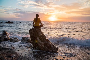 Yoga yapan kadın Lotus pozisyonunda yoga ve meditasyon yapıyor. Akşam okyanusunda açık havada