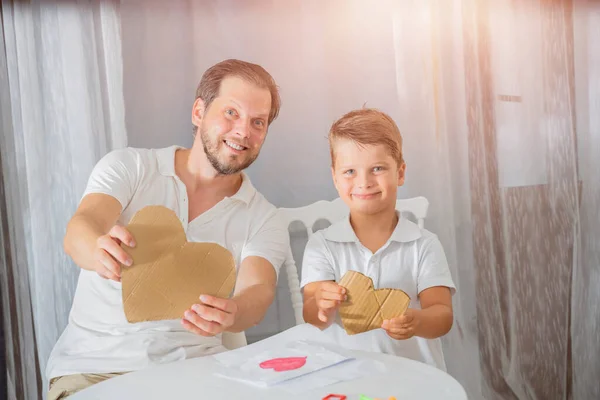 father\'s day, the son makes a gift to his father for the holiday. Happy family adult parent dad and small son having fun at home