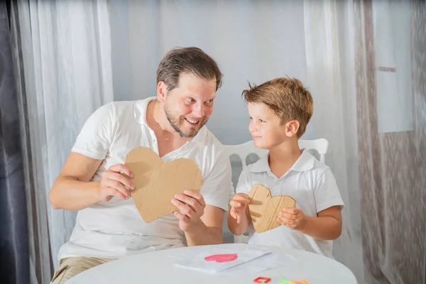father\'s day, the son makes a gift to his father for the holiday. Happy family adult parent dad and small son having fun at home