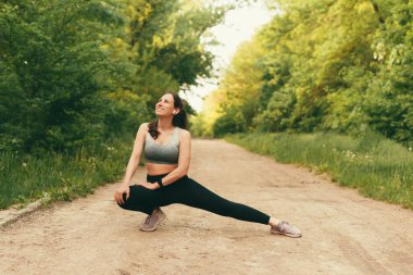 Neşeli genç bayan koşmadan önce parkta esnemenin tadını çıkarıyor..