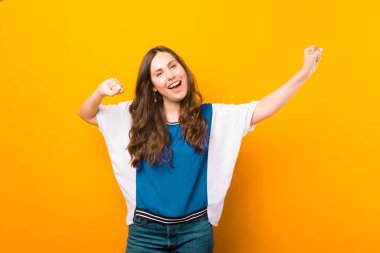 Neşeli genç bayan sarı arka planda kameraya gülümserken kazanan jesti yapıyor..