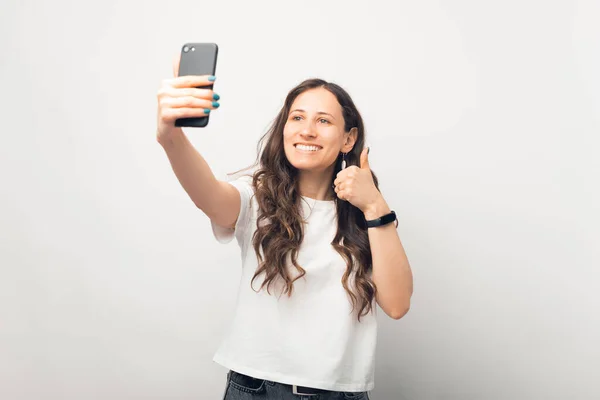 Gyönyörű Csinál Egy Szelfit Telefonjával Miközben Mutatja Hüvelykujját Fel Fehér — Stock Fotó