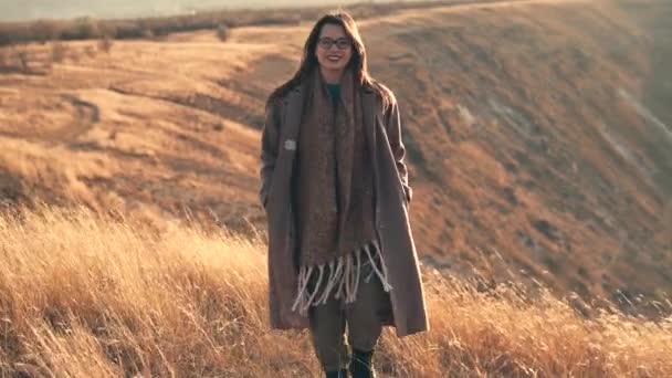 Filmato di una giovane donna sorridente che cammina sulle colline durante il tramonto in autunno — Video Stock
