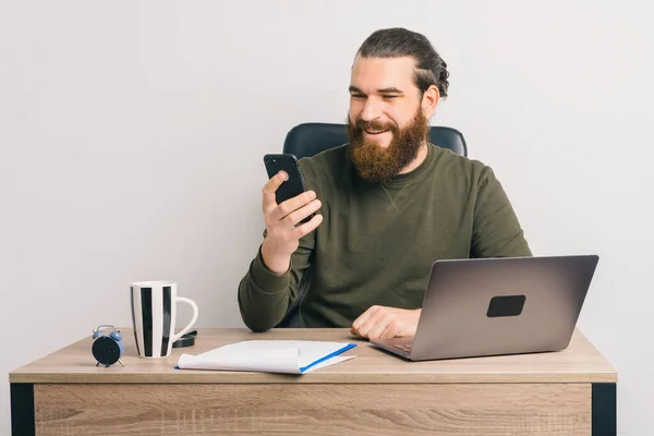 Alegre Barbudo Hombre Sonríe Mientras Está Utilizando Teléfono Portátil Oficina —  Fotos de Stock