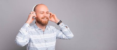 Neşeli ve gülümseyen tişörtlü genç adam beyaz kulaklıklara müzik dinliyor..