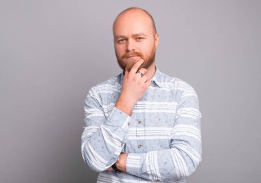 Sakallı, sakallı ve gri arka plandaki kameraya bakan genç adamın fotoğrafı..