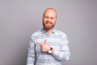 Gri arkaplanı işaret eden sakallı, hoş, genç bir adam..