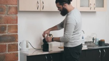 Ofis mutfağında kapsül kahve makinesiyle kahve yapan sakallı genç bir adamın görüntüsü.