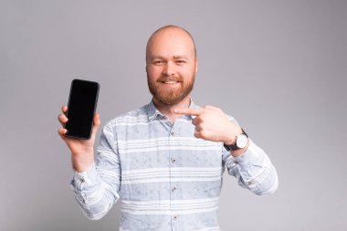 Yakışıklı, neşeli, sakallı adam gri arka planda gezici ekrana bakıyor.