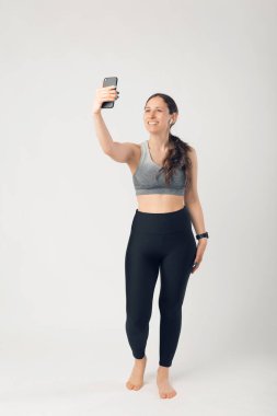 Spor kadının beyaz duvardan selfie çektiği uzun bir fotoğraf.
