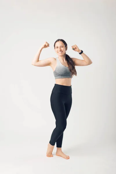 Foto de altura completa de la joven deportista, en ropa deportiva, posando y mostrando sus bíceps —  Fotos de Stock