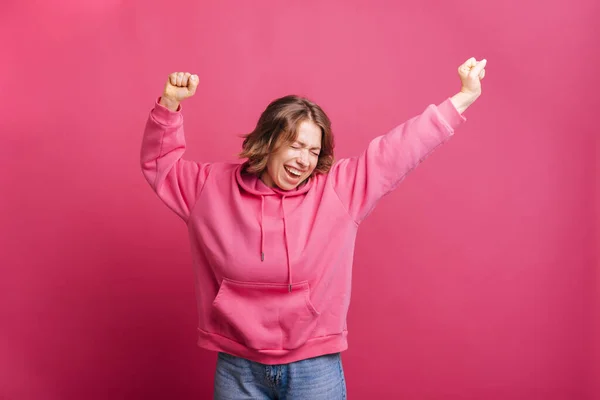 穿着粉色连帽衫的年轻貌美的女人跳过粉色的背景庆祝一番 — 图库照片