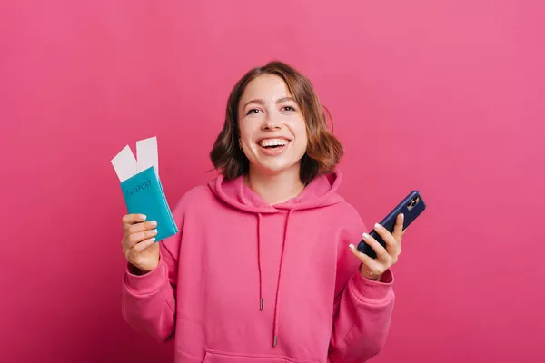 Joyful young smiling woman holding passport with tickets and smartphone, ready for travel — Stock Photo, Image