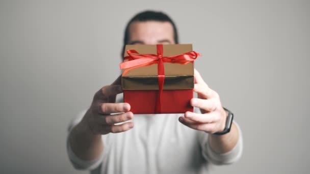 Πλάνα από χαρούμενα γενειοφόρος hipster άνθρωπος κρατώντας κόκκινο κουτί δώρου πάνω από γκρι φόντο — Αρχείο Βίντεο
