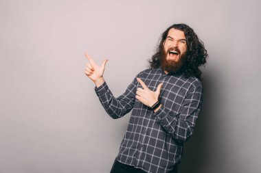 Gri arkaplandaki boşluğu işaret eden çığlık atan sakallı adam.