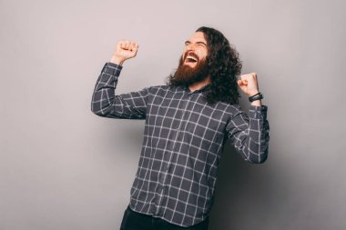 Şaşırmış sakallı adam gri arka plandaki zaferi kutluyor.