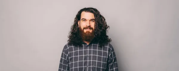 Portré fiatal jóképű szakállas férfi hosszú göndör haj néz a kamera felett szürke háttér — Stock Fotó