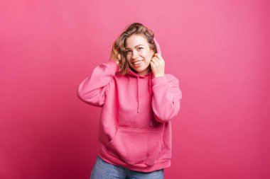 Mutlu kadın pembe kapüşonlu pembe kapüşonlu bir duvarın yanında kameraya gülümsüyor. .