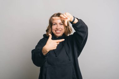 Siyah kapüşonlu genç mutlu kızın gri arka planda fotoğraf jesti yaptığı fotoğraf..