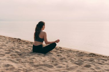 Genç bir kadın kumsalda meditasyon yapıyor güneşli günün tadını çıkarıyor.