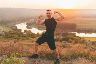 Kaslı genç adam, güneşli bir tepede ne kadar güçlü olduğunu gösteriyor.