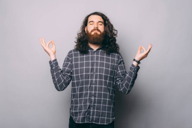 Kareli gömlekli genç adam gri arka planda zen hareketi yapıyor.