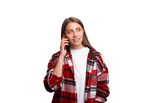 Фото молодой женщины в красной клетчатой рубашке, говорящей на смартфоне, изолированном на белом — стоковое фото