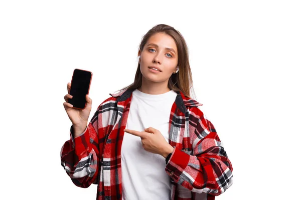 Foto de uma jovem mulher de camisa quadriculada vermelha apontando para o smartphone — Fotografia de Stock