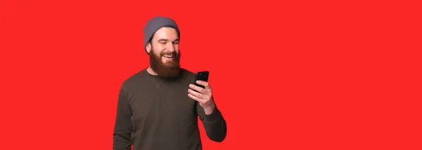 Banner μέγεθος φωτογραφία του νεαρού χαρούμενα γενειοφόρος hipster άνθρωπος χρησιμοποιώντας smartphone και χαμογελώντας — Φωτογραφία Αρχείου