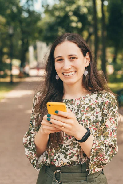 城市公园里，一个微笑的年轻女子在户外用智能手机拍摄的垂直照片 — 图库照片
