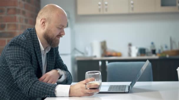 Footage of young handsome bearded man sitting in office at laptop and drinking cup of coffee — Stock Video