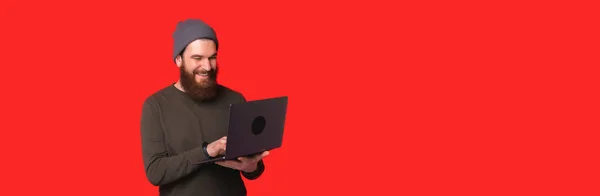 Pria tersenyum menggunakan laptop dekat latar belakang merah — Stok Foto