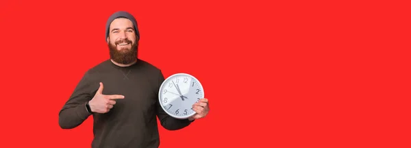 Lächelnder Mann zeigt auf runde Uhr auf hellem Hintergrund — Stockfoto