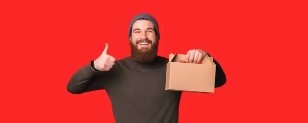 Lächelnder Mann zeigt Daumen nach oben, während er Kartonverpackung empfiehlt — Stockfoto