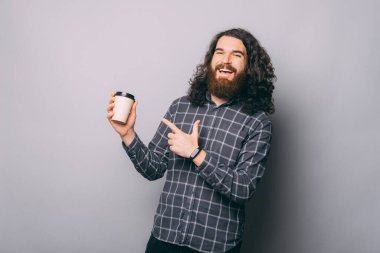 Sakallı bir adamın elinde kahve tutarken ve onu gri arka planda tutarken fotoğrafı.