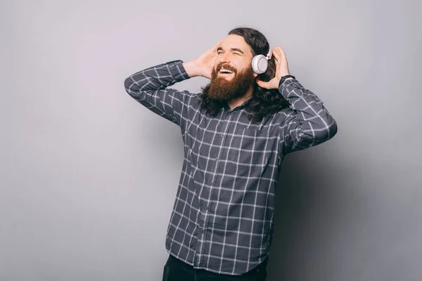 Fröhlicher Mann hört Musik mit modernen Kopfhörern und schaut weg, während er auf grauem Hintergrund steht — Stockfoto