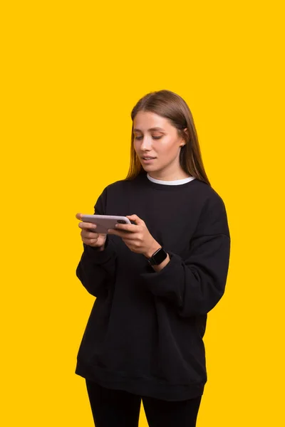 Fénykép a lány tizenéves játék online játékok mobiltelefon sárga háttér — Stock Fotó