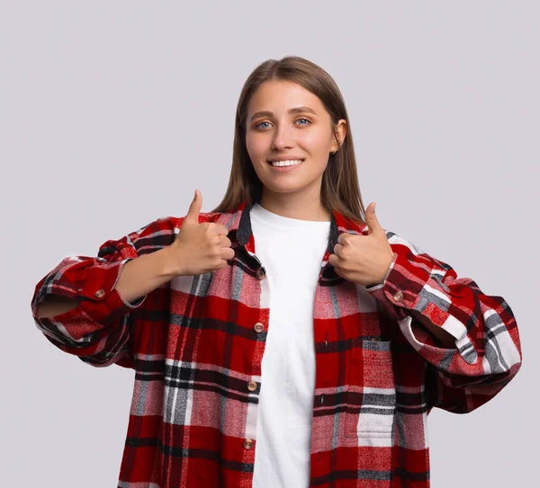 Мотивированная привлекательная молодая женщина подает большой палец вверх жест одобрения и успеха с улыбкой — стоковое фото